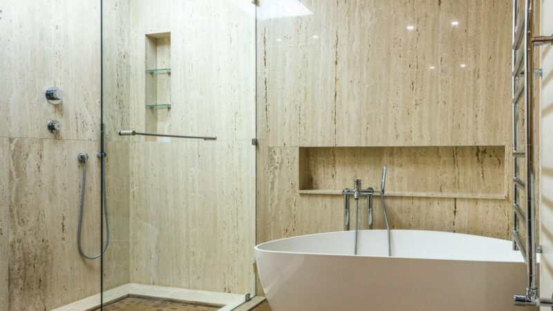 Contemporary bathroom featuring a marble wall, glass shower, and stylish bathtub.